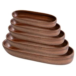 A rustic acacia wood boat serving tray filled with fresh green salad and sliced heirloom tomatoes.